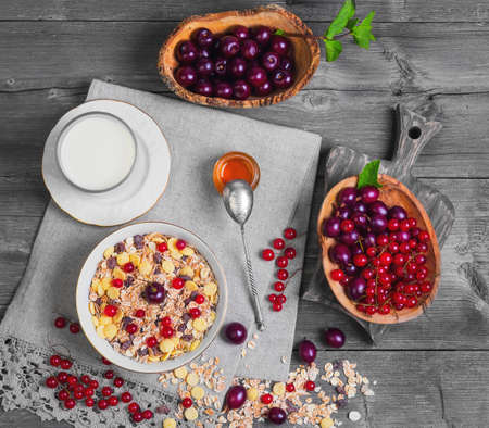 Morning breakfast muesli mix cereals, dried fruits, berries in bowl. Fresh red berries to muesli cereals cherries, gooseberries, redcurrants, honey, milk. Muesli, berries scattered on table. Top viewの写真素材