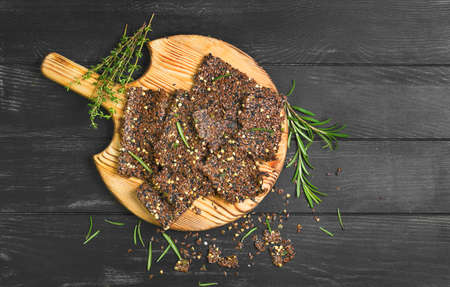 Bread crackers from grain flax seeds, sesame, spices, wooden board, healthy food. Broken pieces grain Bread crackers flax seeds. Spices for flax crackers grain breads. Black background, top viewの写真素材