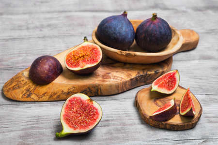 Violet Blue figs whole fruit, figs cut into pieces on a board of wood of olive, light white wooden backgroundの写真素材