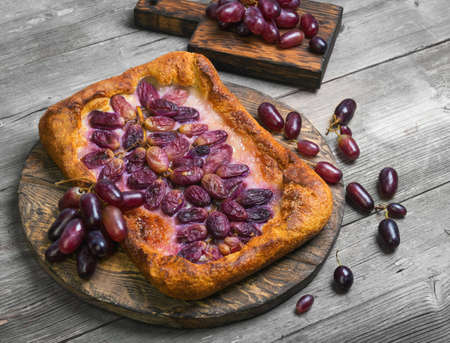 Homemade Galette or crusty pie with purple grapes. Grapes for pie on board. Grapes on the table. Gray wooden background.の写真素材