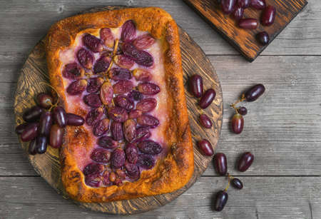 Homemade Galette or crusty pie with purple grapes. Grapes for pie on board. Grapes on the table. Gray wooden background. Top viewの写真素材
