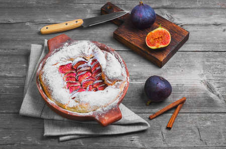 Tart pie with figs and powdered sugar. Fresh fruits purple figs for pie on board. Cut figs, cinnamon. Gray wooden background table, knife.の写真素材