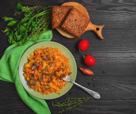 Vegetarian lunch stewed braised cabbage with mushrooms, carrots. Herbs spices for cabbage stewed with mushrooms parsley, thyme, pepper, cherry tomatoes, onions, grain bread. Stewed cabbage on fork. Top viewの写真素材