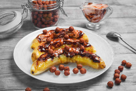 Bananas baked grilled cottage cheese sauce with ice cream chocolate, white plate. Chocolate cereal balls, chocolate sauce ice cream cottage cheese in glass  bowl. Light wooden table background.の写真素材