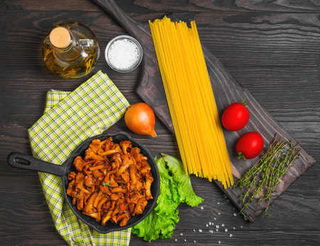 Raw not cooked Pasta spaghetti Tagliatelle with mushrooms chanterelles. Mushrooms, chanterelles pasta. Ingredients for pasta spaghetti mushrooms tomatoes, thyme, oil. Dark wooden background. Top viewの写真素材