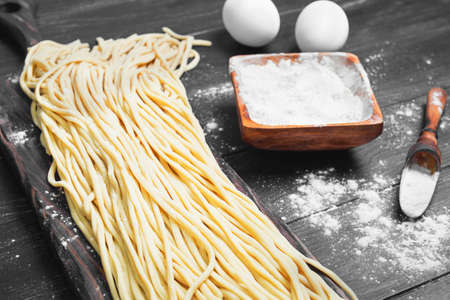 Homemade Uncooked pasta spaghetti noodles on board. Ingredients for home-made spaghetti noodles chicken eggs, flour. The dark black wood background.の写真素材