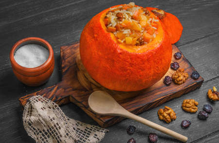 Halloween Pumpkin risotto with raisins. Rice porridge with sweet pumpkin, raisins, nuts. Baked pumpkin Halloween for rice. Sugar, dark wooden background.の写真素材