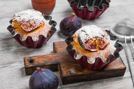 Baked Muffins cake with figs, sugar powder. Fresh fruit muffin figs. Metal molds for muffins, cinnamon, board. Light white wooden background.の写真素材