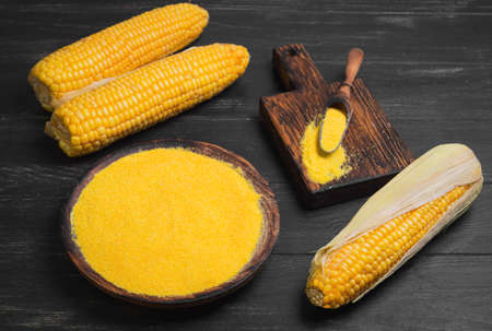Fresh Corn and corn grits polenta in wooden bowl on wooden black table background. Corn grits polenta in wooden spoon. Not cooked corn polenta.の写真素材