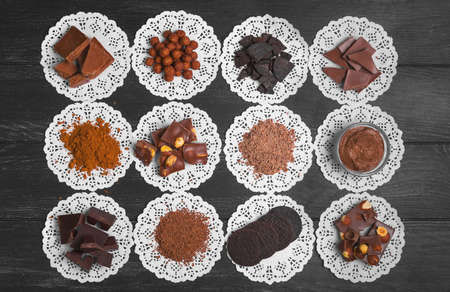 Chocolate assortment, ingredients, texture. Cocoa powder, cocoa mass chocolate, paste chocolate, candy, chocolate cookies, broken chocolate, almonds hazelnuts Dark black wooden background Top viewの写真素材