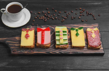 Breakfast for men. Figured sandwiches, coffee. Sausage sandwiches, cheese, vegetables. Concept Breakfast for the day men, father's day, business lunch. Dark black wood background.の写真素材