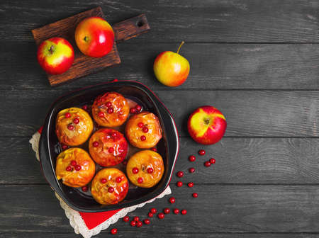 Baked apples baking in oven. Fresh apples for baking on board. Sauce for baked apples, red berries. Dark black wood background. Garden apples. Top view, blank space.の写真素材