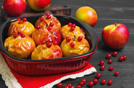 Baked apples baking in oven. Fresh apples for baking on board. Caramel sauce for baked apples, red berries. Dark black wood background. Garden apples.の写真素材