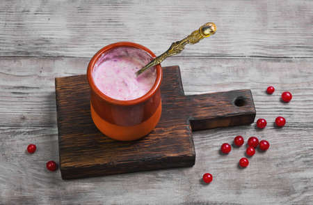 Ceramic cup bowl with of homemade berry yogurt, board. Red berries of cranberry, lingonberry for making homemade yogurt. Light white wooden rustic background.の写真素材