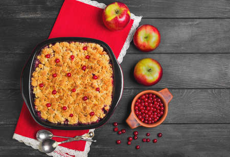 Dessert pie crumble cake apples, red berries cranberries. Fresh apples, berries for  pie crumble cake, cloth. Red Black ceramic baking pan cake crumble. Wooden dark background. Top view blank space.の写真素材