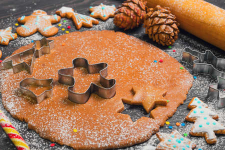 Cooking Christmas cookies gingerbread. On a dark brown background gingerbread dough. Forms for Christmas cookies gingerbread, rolling pin, cones. Cookies with icing. Christmas New Year card.の写真素材