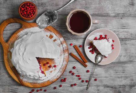 Christmas New Year winter pie cake, red berry cranberries, cover white whipped meringue icing, tea. Slice winter Christmas pie cake on plate. Cranberry for winter pie. Light wood background. Top viewの写真素材