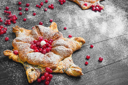 Homemade Sweet pastry buns in form of Christmas snowflakes, powdered sugar. Dark black wood background. Concept snow for Christmas cards. Red berries of cranberry buns for snowflakes.の写真素材