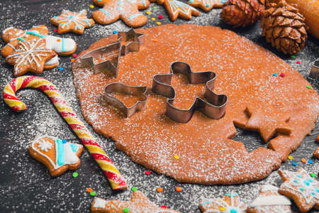 Cooking Christmas cookies gingerbread. On a dark brown background gingerbread dough. Forms for Christmas cookies gingerbread, rolling pin, cones. Cookies with icing. Christmas New Year card.の写真素材