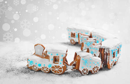 New Year card with Christmas sweets toy. Gingerbread cookie in the form a Christmas train. Gingerbread Christmas tree on the train. Snow background with snowflakes, blue, white icing on steam train.の写真素材