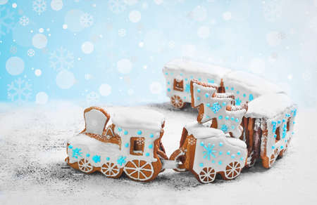 New Year card with Christmas sweets toy. Gingerbread cookie in the form a Christmas train. Gingerbread Christmas tree on the train. Snow background with snowflakes, blue, white icing on steam train.の写真素材
