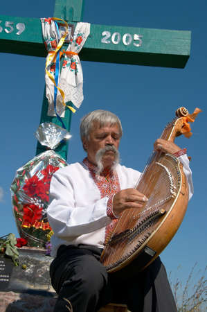 Senior ukrainian musician with bandura under cross against deep blue skyの写真素材