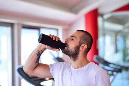 Young adult man drinking bottle of water on trreadmill in gym.の写真素材