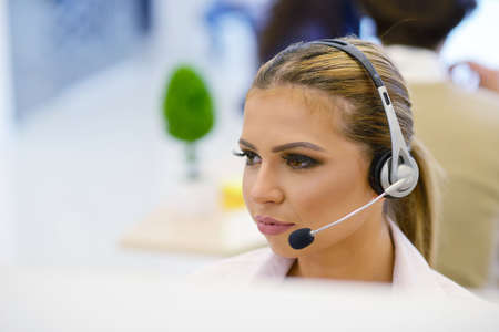 Portrait of a beautiful business woman with braces on the teeth, sitting at the desk and with headphonesの写真素材