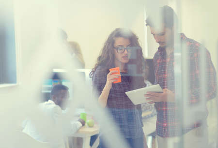young startup business people, couple working on tablet computer, businesspeople group on meeting in background at office interiorの写真素材