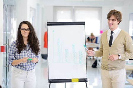 Businessman giving a presentation to his colleagues at work standing in front of a flipchart with notes and diagramsの写真素材