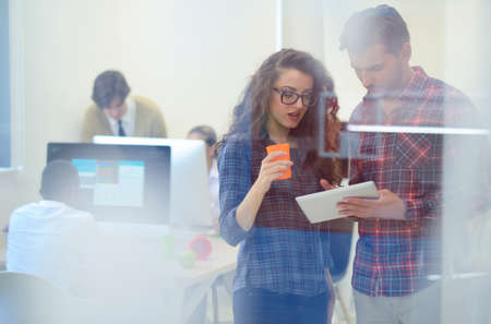 young startup business people, couple working on tablet computer, businesspeople group on meeting in background at office interiorの写真素材