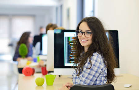 Casual caucasian businesswoman at business startup office with pen in hand, wearing glasses. Looking at camera, scarf around neck.の写真素材