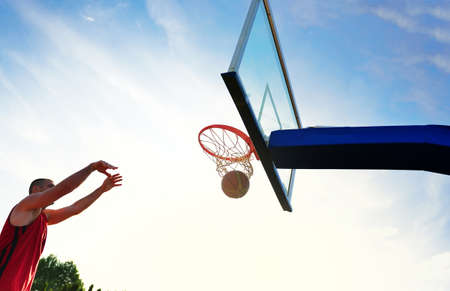 Young basketball player drives to the hoop for a high flying slam dunk in front of sunset skyの写真素材
