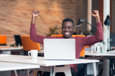 Happy smiling successful African American businessman in a modern startup office indoorsの写真素材
