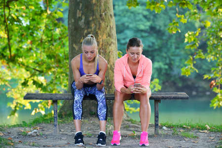 Shot of two females taking a quick break while out for a trail run using phone.の写真素材