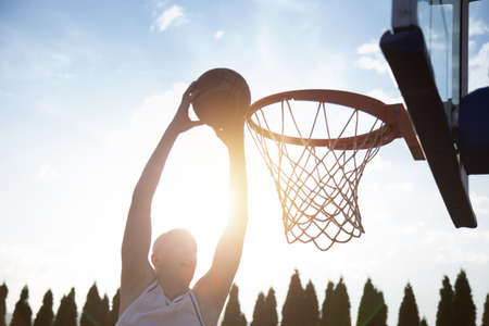 Young man jumping and making a fantastic slam dunk playing streetball, basketball. Urban authentic.