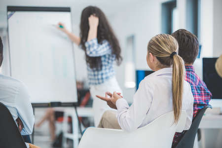 Businessman giving a presentation to his colleagues at work standing in front of a flipchart with notes and diagramsの写真素材
