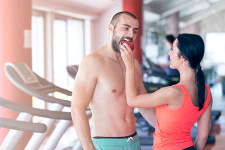 Happy couple in gym feeding each other with apple.の写真素材