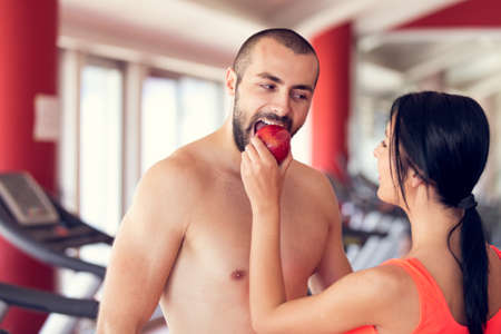 Happy couple in gym feeding each other with apple.の写真素材
