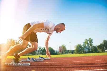 Male athlete on starting position at athletics running track. Runner practicing his sprint start in...