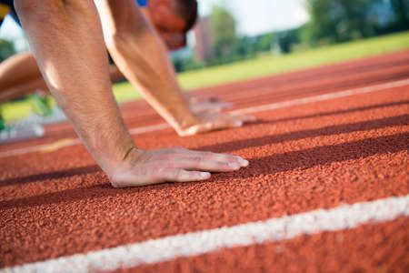 Close-up side view of cropped people ready to race on track field.