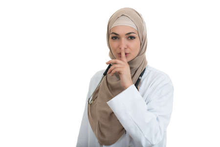 Closeup portrait of friendly, confident muslim with hijab doctor showing shh sigh, silence, healthcare professional isolated on white background.の写真素材