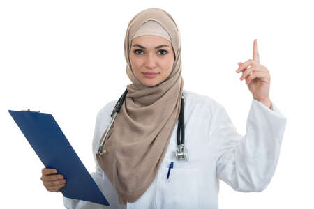 Closeup portrait of friendly, smiling confident Muslim female doctor celebrating success, and pointing arm, healthcare professional isolated on white background.の写真素材