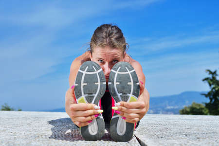 healthy young pretty woman stretching her leg during exercise in park right before a work out....