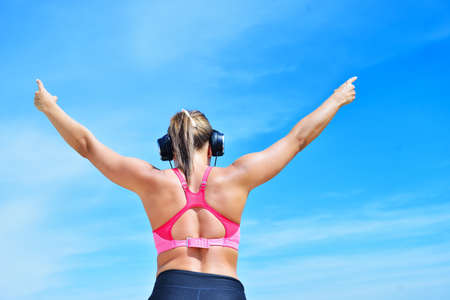 Success fitness winning woman concept with earphones. female athlete runner cheering arms raised up for achievement in weight loss or life goal.の写真素材