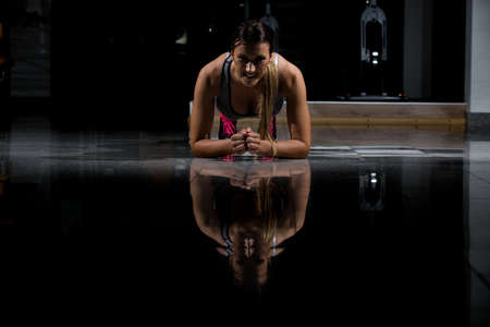 woman in a gym exercising, doing push ups. Dark background.の写真素材
