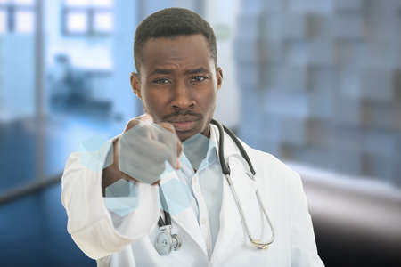 Angry african black male doctor pointing finger at you with stethoscope around his neck, pointing at camera with serious facein modern hospitalの写真素材