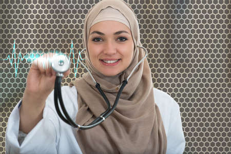 close up portrait of arab female doctor smiling while using stethoscope.の写真素材