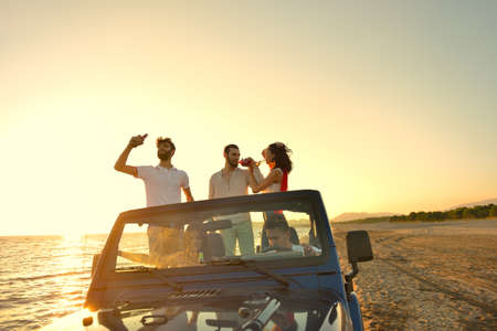 Five young people having fun in convertible car at the beach at sunset.の写真素材