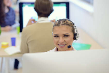 Portrait of a beautiful business woman with braces on the teeth, sitting at the deskの写真素材